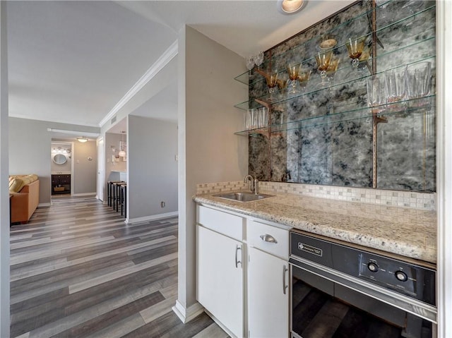 kitchen with light stone counters, wood finished floors, a sink, white cabinets, and crown molding