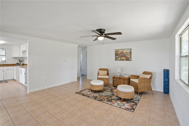 living area with a textured ceiling, light tile patterned floors, and ceiling fan