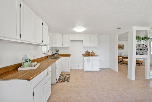 kitchen featuring a textured ceiling, sink, light tile patterned floors, and white cabinets