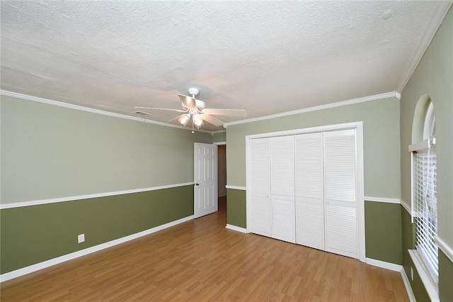 unfurnished bedroom featuring baseboards, ornamental molding, wood finished floors, a closet, and a textured ceiling