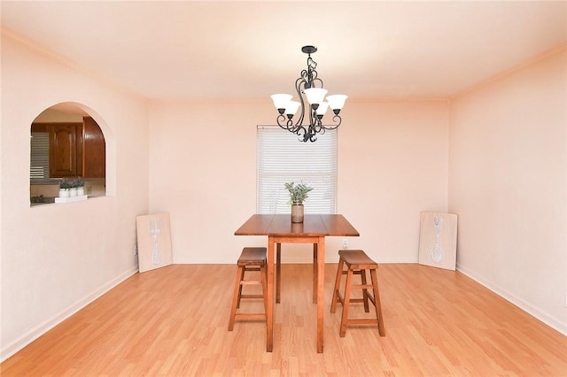 dining area with baseboards, a chandelier, ornamental molding, light wood-style floors, and arched walkways