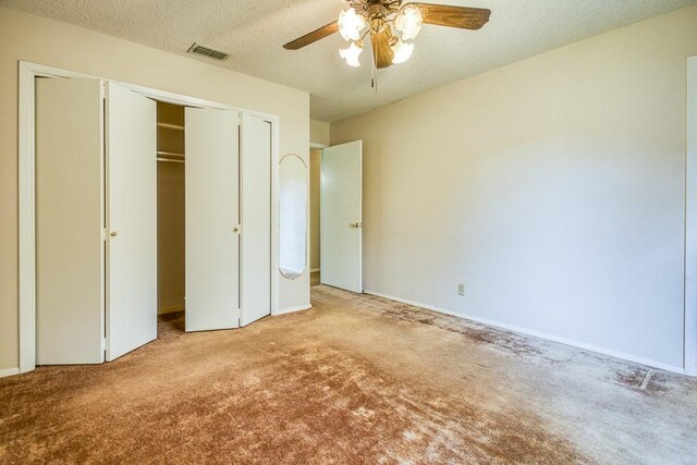unfurnished bedroom with carpet flooring, a closet, a textured ceiling, and a ceiling fan