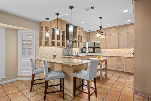 kitchen featuring a kitchen breakfast bar, hanging light fixtures, kitchen peninsula, light stone countertops, and wall chimney range hood