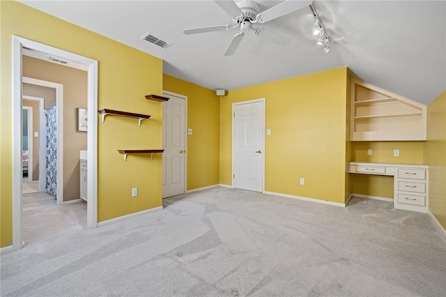 unfurnished bedroom featuring light colored carpet, rail lighting, and built in desk