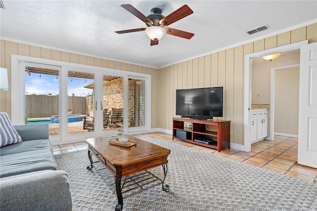 living room featuring crown molding, wooden walls, ceiling fan, and light tile patterned flooring