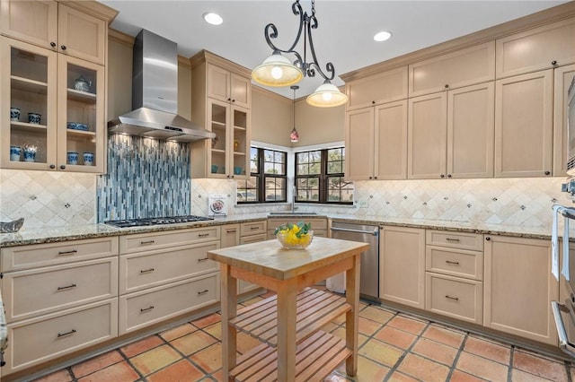 kitchen featuring pendant lighting, light stone countertops, stainless steel appliances, and wall chimney exhaust hood