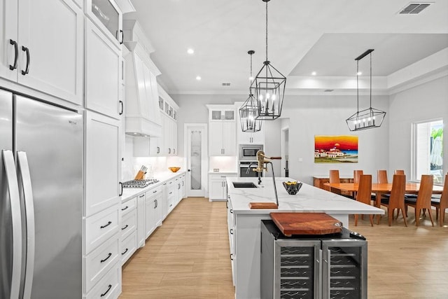 kitchen with appliances with stainless steel finishes, light wood-style floors, a kitchen island with sink, wine cooler, and visible vents