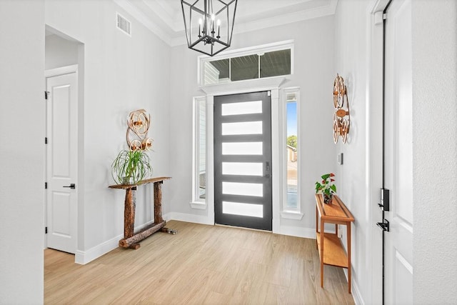 entryway featuring an inviting chandelier, light wood finished floors, baseboards, visible vents, and ornamental molding