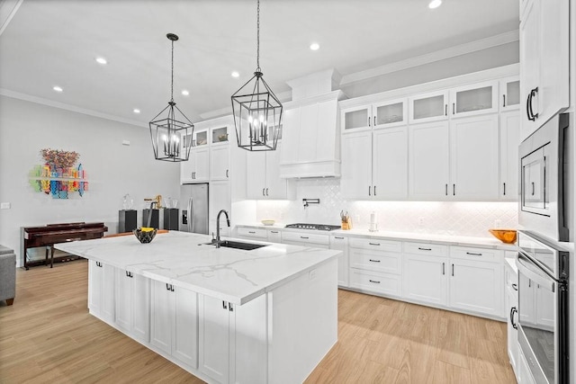 kitchen with a notable chandelier, appliances with stainless steel finishes, a sink, a center island with sink, and ornamental molding