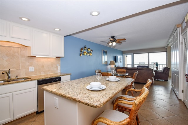 kitchen with a center island, dishwasher, sink, a breakfast bar area, and light stone countertops