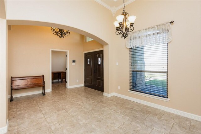 foyer with baseboards, arched walkways, a towering ceiling, crown molding, and a chandelier