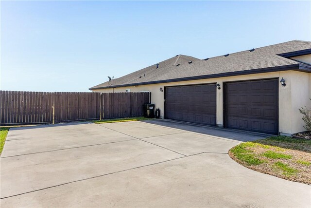 view of side of home featuring stucco siding, driveway, a shingled roof, and fence