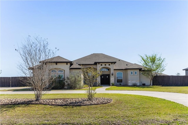 mediterranean / spanish-style house featuring stucco siding, curved driveway, a front lawn, and fence