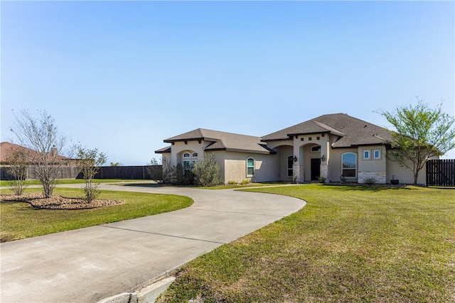 mediterranean / spanish house with a front lawn, stucco siding, fence, and curved driveway