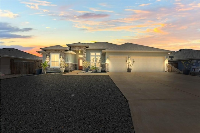 prairie-style house featuring stucco siding, fence, a garage, driveway, and stone siding