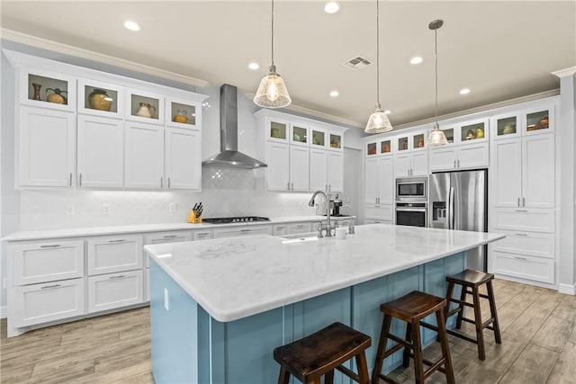 kitchen featuring light wood-style flooring, a sink, visible vents, stainless steel appliances, and wall chimney exhaust hood