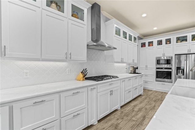 kitchen with wall chimney range hood, decorative backsplash, white cabinets, stainless steel appliances, and light wood finished floors