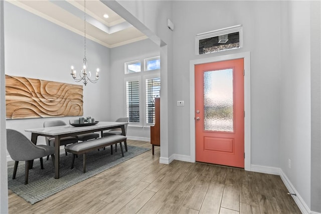 entryway featuring a chandelier, baseboards, light wood-type flooring, ornamental molding, and a high ceiling