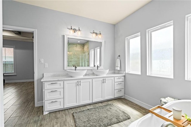 full bathroom with a freestanding bath, double vanity, a sink, baseboards, and a stall shower