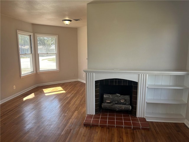 unfurnished living room with dark wood-style floors, a tile fireplace, visible vents, and baseboards