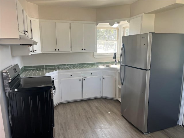 kitchen featuring tile counters, freestanding refrigerator, white cabinetry, a sink, and range with electric cooktop