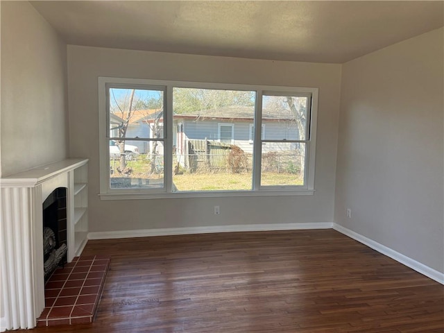 unfurnished living room featuring baseboards, dark wood finished floors, and a tiled fireplace