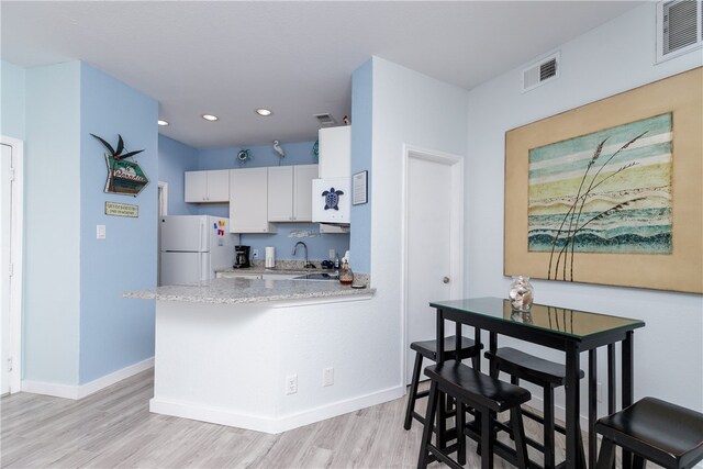 kitchen featuring white cabinetry, kitchen peninsula, light hardwood / wood-style floors, and white fridge