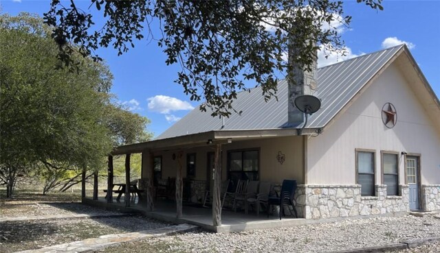 197 N Tomahawk Way, Concan, TX 78838 - back of property featuring stone siding, metal roof, a patio, and a chimney