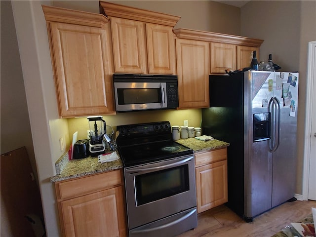 kitchen featuring light wood-type flooring, light brown cabinetry, light stone counters, and appliances with stainless steel finishes