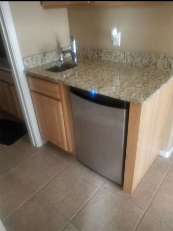 kitchen featuring dishwasher, light stone counters, sink, and light tile patterned floors