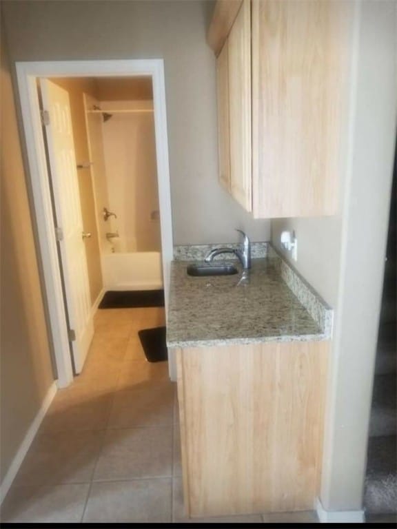 kitchen featuring light tile patterned floors, light brown cabinetry, sink, and light stone counters