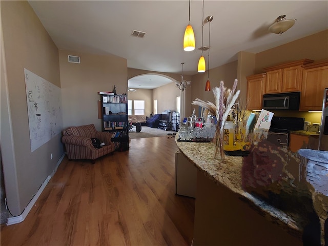 kitchen featuring black electric range, dark wood-type flooring, hanging light fixtures, and light stone counters