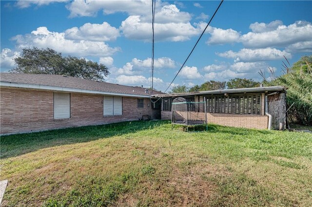 445 Troy Dr, Corpus Christi, TX 78412 - rear view of property featuring a trampoline, a lawn, and brick siding