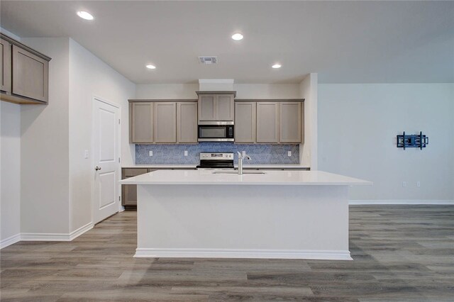 kitchen featuring light wood-type flooring, stainless steel appliances, a center island with sink, and backsplash