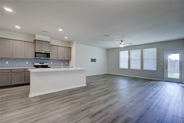 kitchen with backsplash, stainless steel appliances, ceiling fan, a center island with sink, and light hardwood / wood-style floors