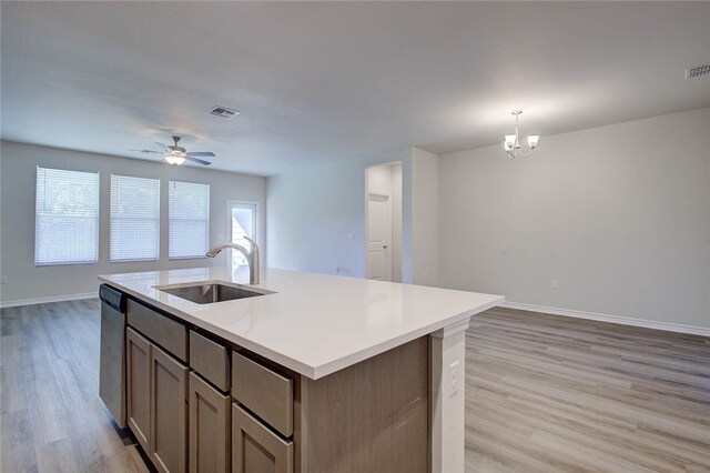 kitchen featuring sink, stainless steel dishwasher, light wood-type flooring, an island with sink, and decorative light fixtures