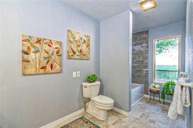 bathroom with toilet, a tub, a textured ceiling, and baseboards