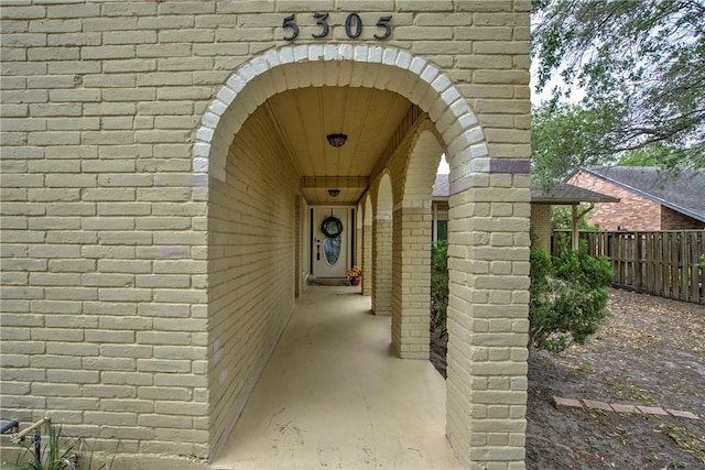 doorway to property featuring brick siding and fence