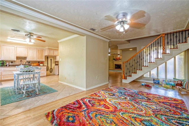 living room featuring stairway, a textured ceiling, ornamental molding, and ceiling fan