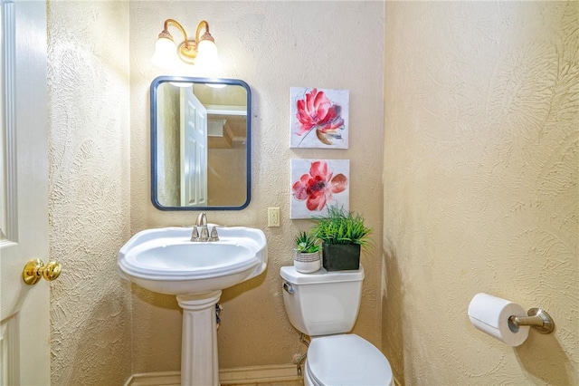 bathroom featuring toilet, a textured wall, and baseboards
