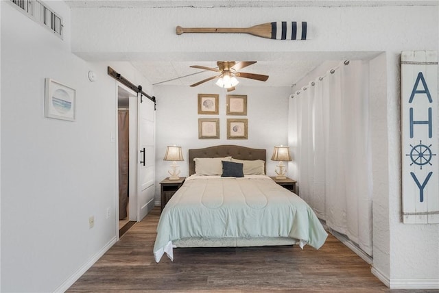 bedroom with a barn door, wood finished floors, a ceiling fan, visible vents, and baseboards