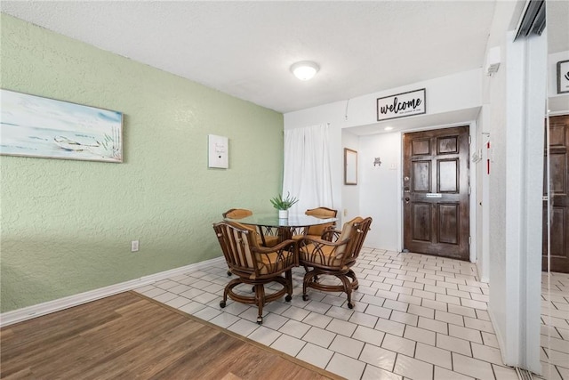 dining space with light wood-type flooring, baseboards, and a textured wall