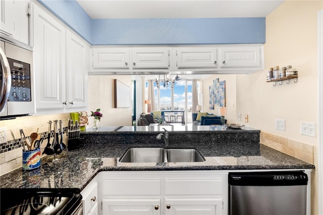 kitchen featuring stainless steel appliances, sink, an inviting chandelier, dark stone countertops, and white cabinetry