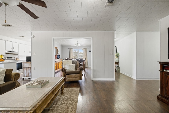 living room featuring wood walls, dark wood-type flooring, and ceiling fan