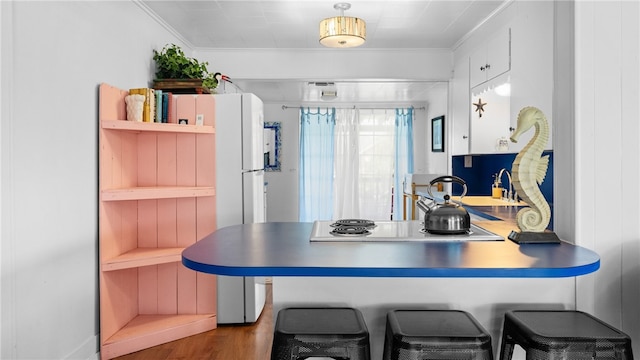 kitchen featuring white cabinets, wood finished floors, a peninsula, crown molding, and electric stovetop