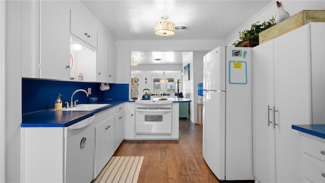 kitchen featuring white appliances, dark countertops, ornamental molding, wood finished floors, and a sink