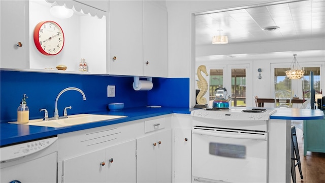 kitchen featuring a peninsula, white appliances, a sink, white cabinets, and a wealth of natural light