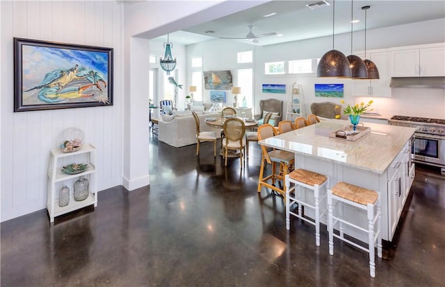 126 Reserve Ln, Rockport, TX 78382 - kitchen with stainless steel stove, a kitchen breakfast bar, a ceiling fan, light stone counters, and white cabinetry