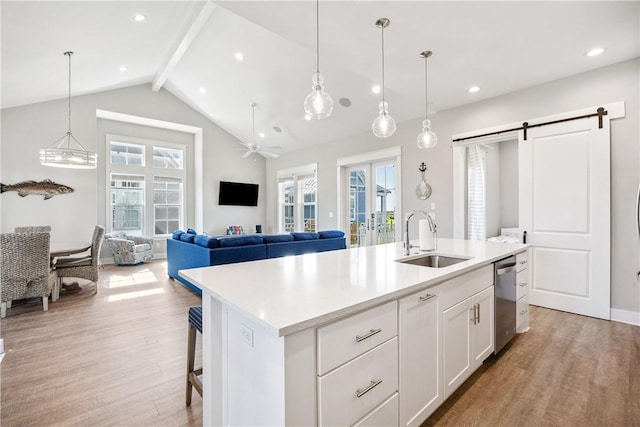 kitchen with sink, a barn door, an island with sink, light hardwood / wood-style floors, and white cabinetry