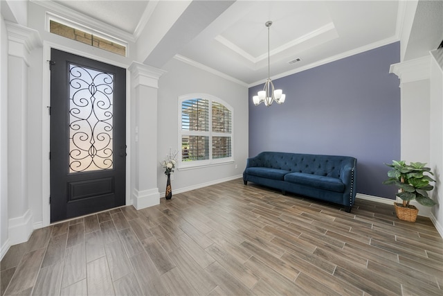 foyer with a chandelier, ornamental molding, ornate columns, hardwood / wood-style floors, and a tray ceiling